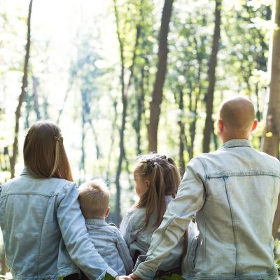 man and woman holding hands together with boy and girl looking at green trees during day